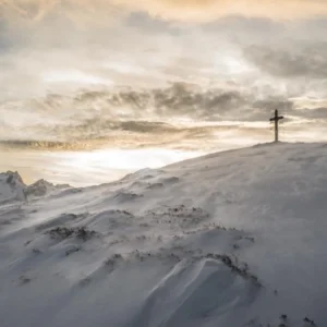Cross standing on a snowy mountain peak under a bright sky