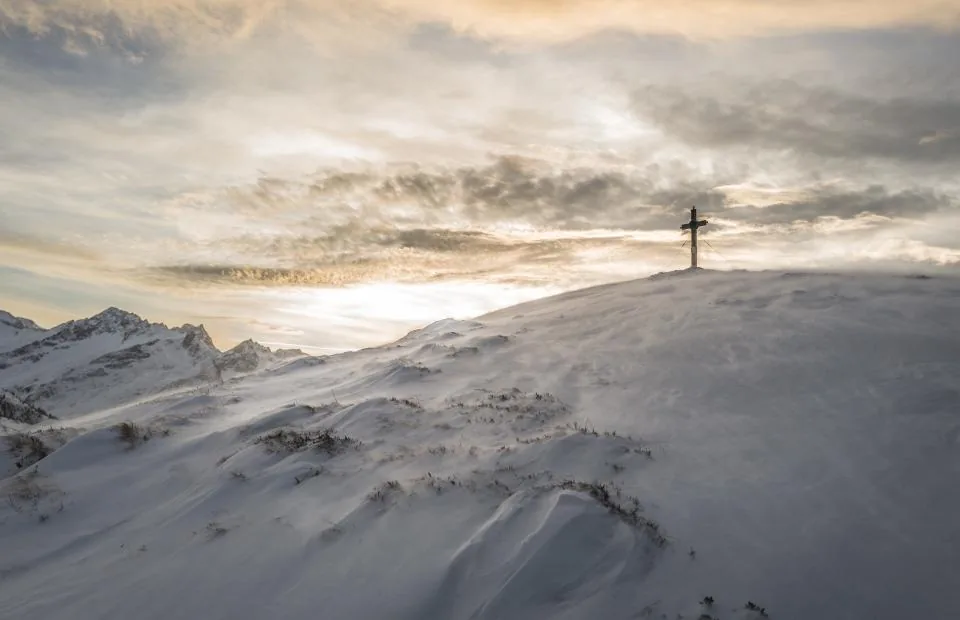 Cross standing on a snowy mountain peak under a bright sky