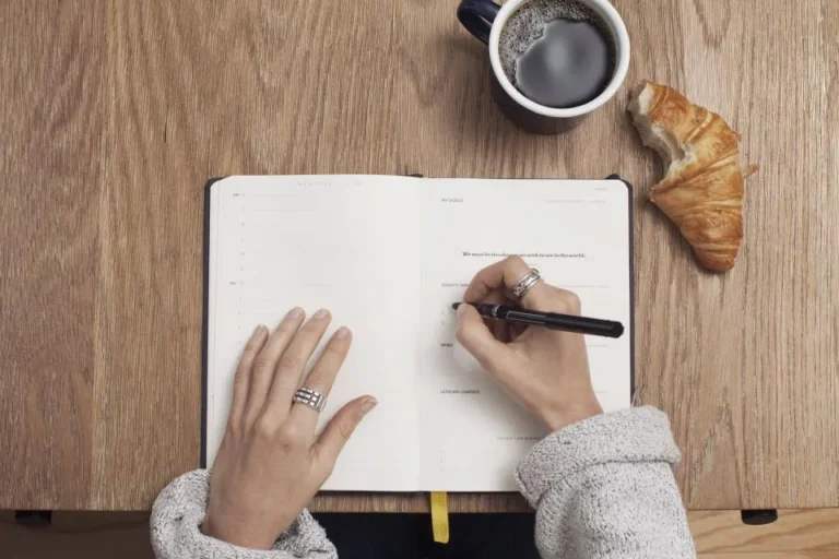 Open journal with coffee and a croissant on a wooden table