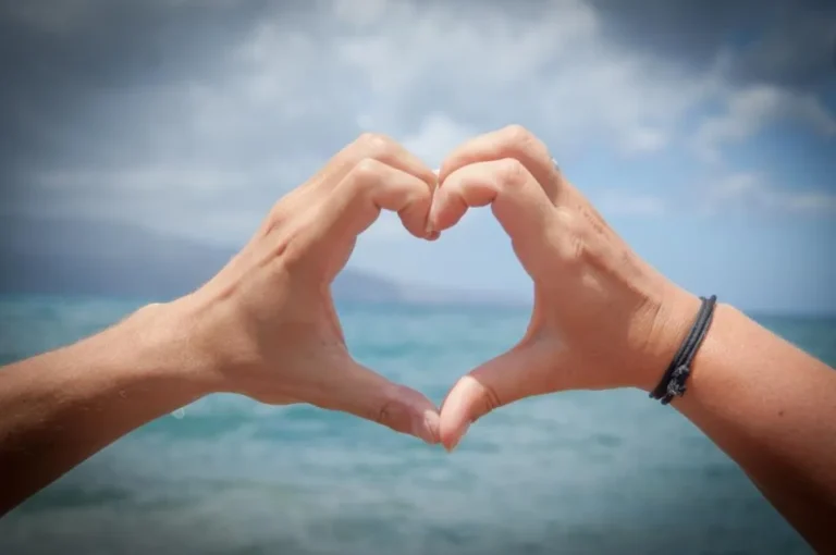 Two hands making a heart shape over the sea