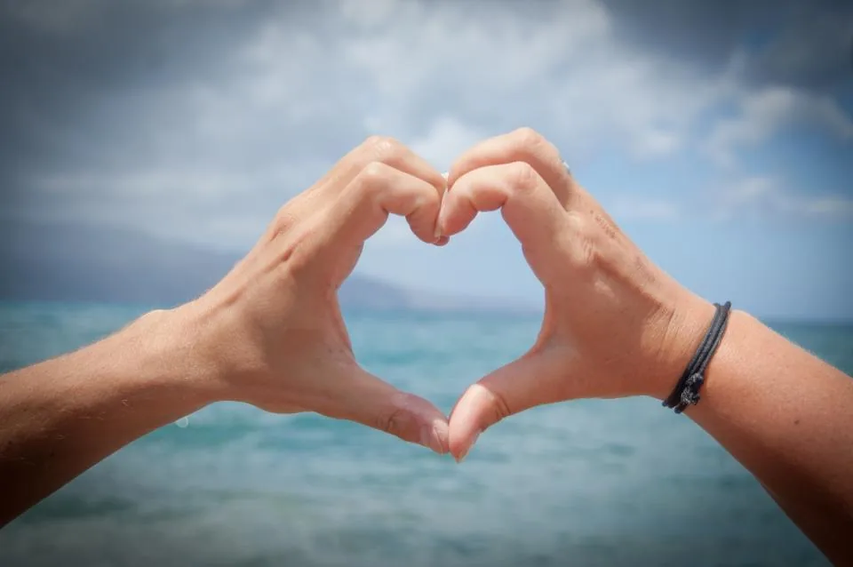 Two hands making a heart shape over the sea