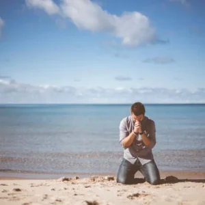 Man kneeling in morning prayer on a quiet beach