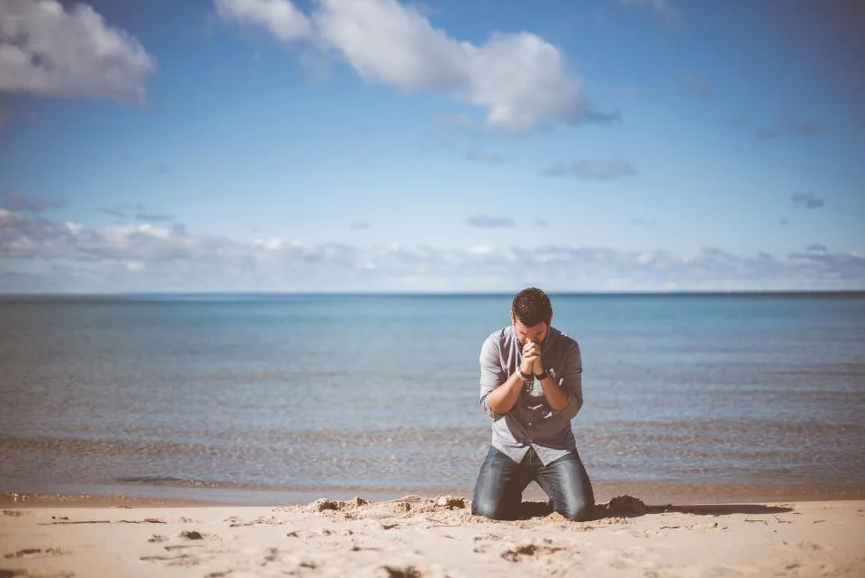 Man kneeling in morning prayer on a quiet beach