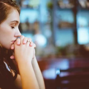 Young woman praying quietly with folded hands