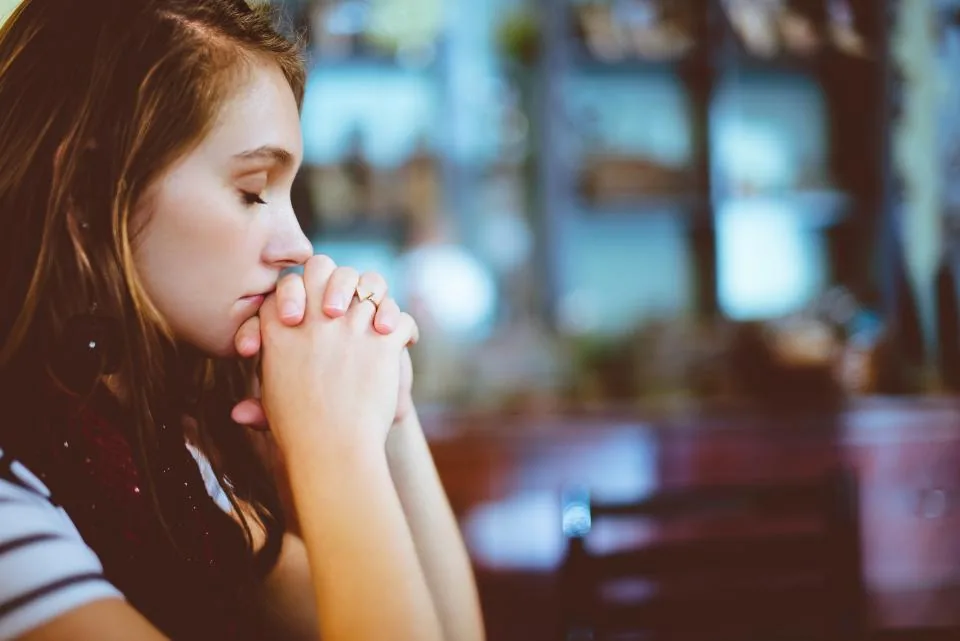 Young woman praying quietly with folded hands